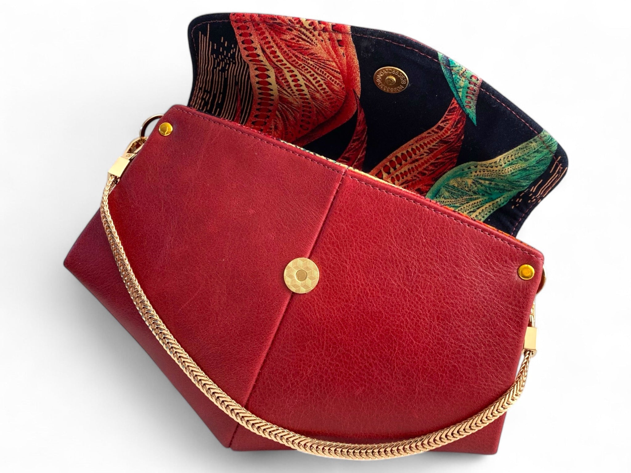 Red leather handbag with gold chain and decorative interior lining on a white background