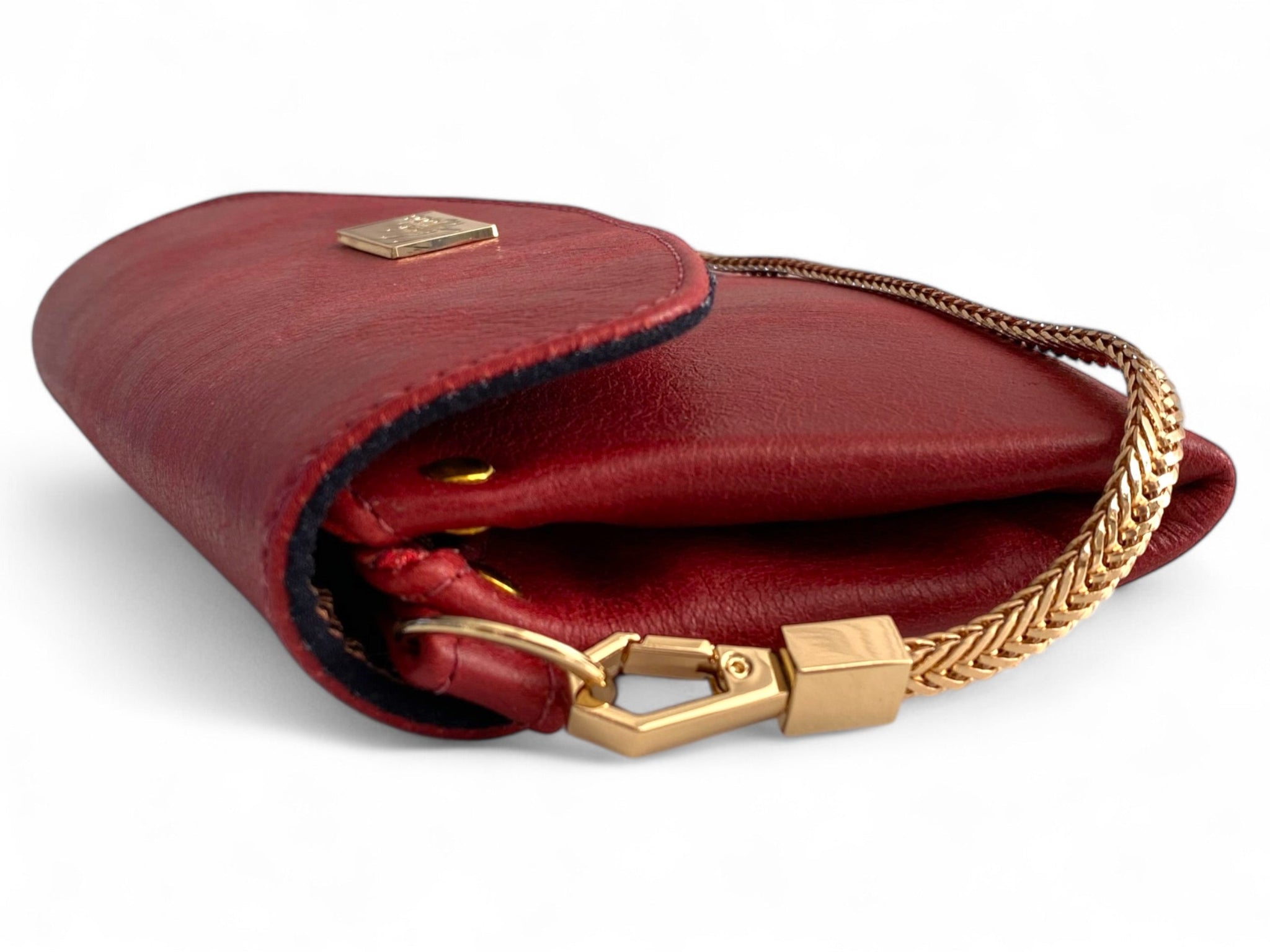 Side view of a red leather clutch bag with gold clasp and chain on white background