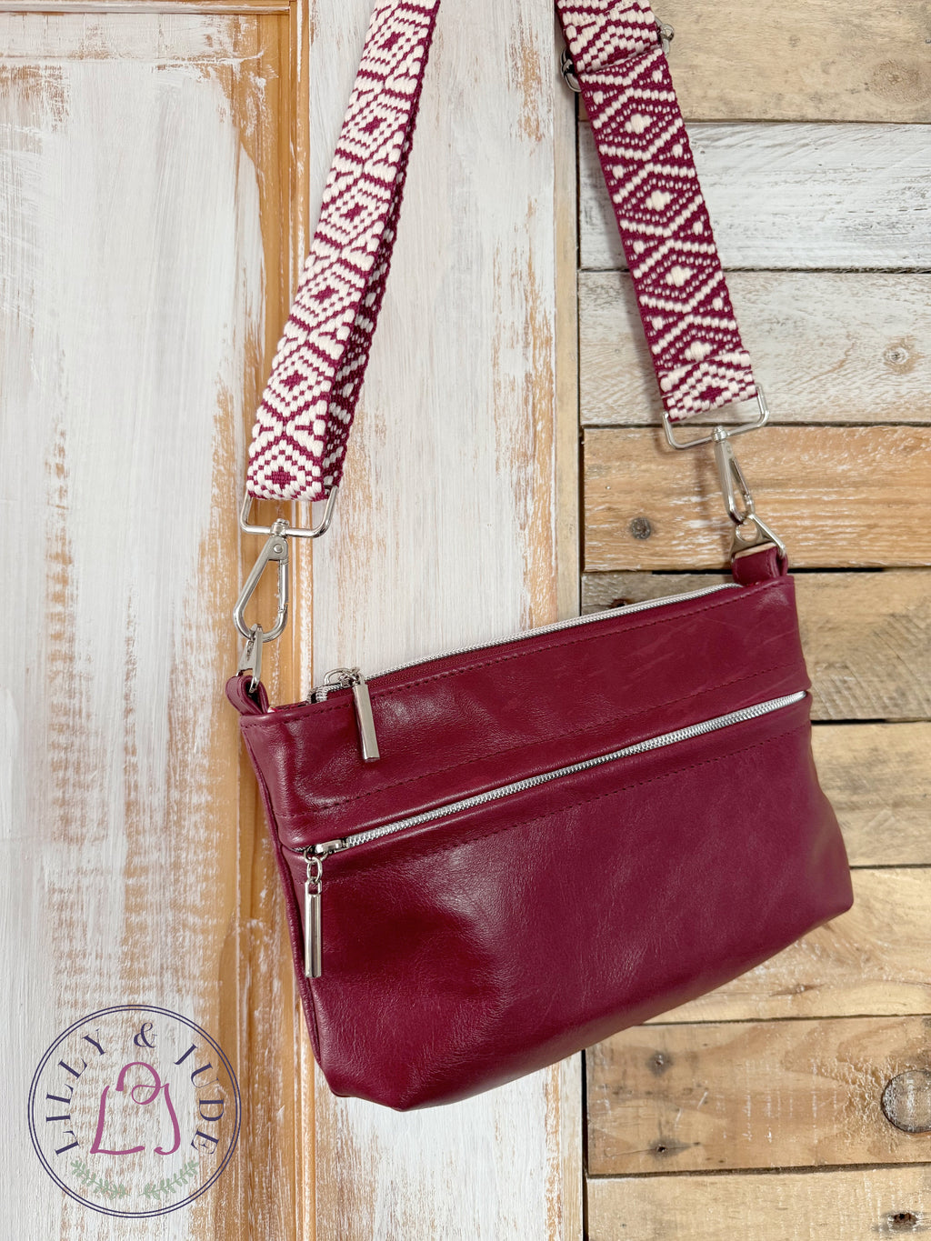 Burgundy leather crossbody bag with woven crossbody strao and silver hardware, hanging on a rustic wooden door
