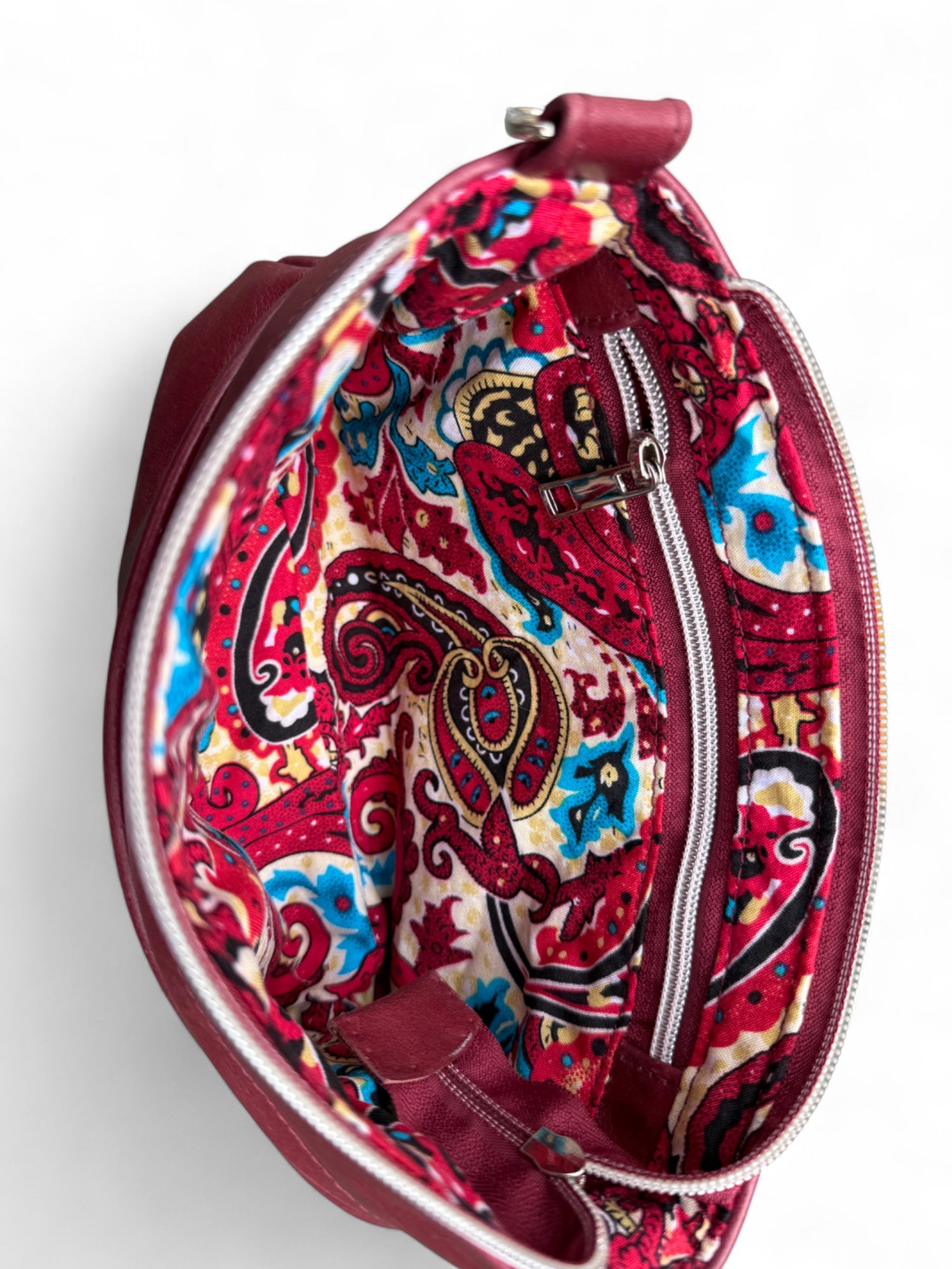 Open view of red leather crossbody bag, revealing a vibrant  paisley patterned lining
