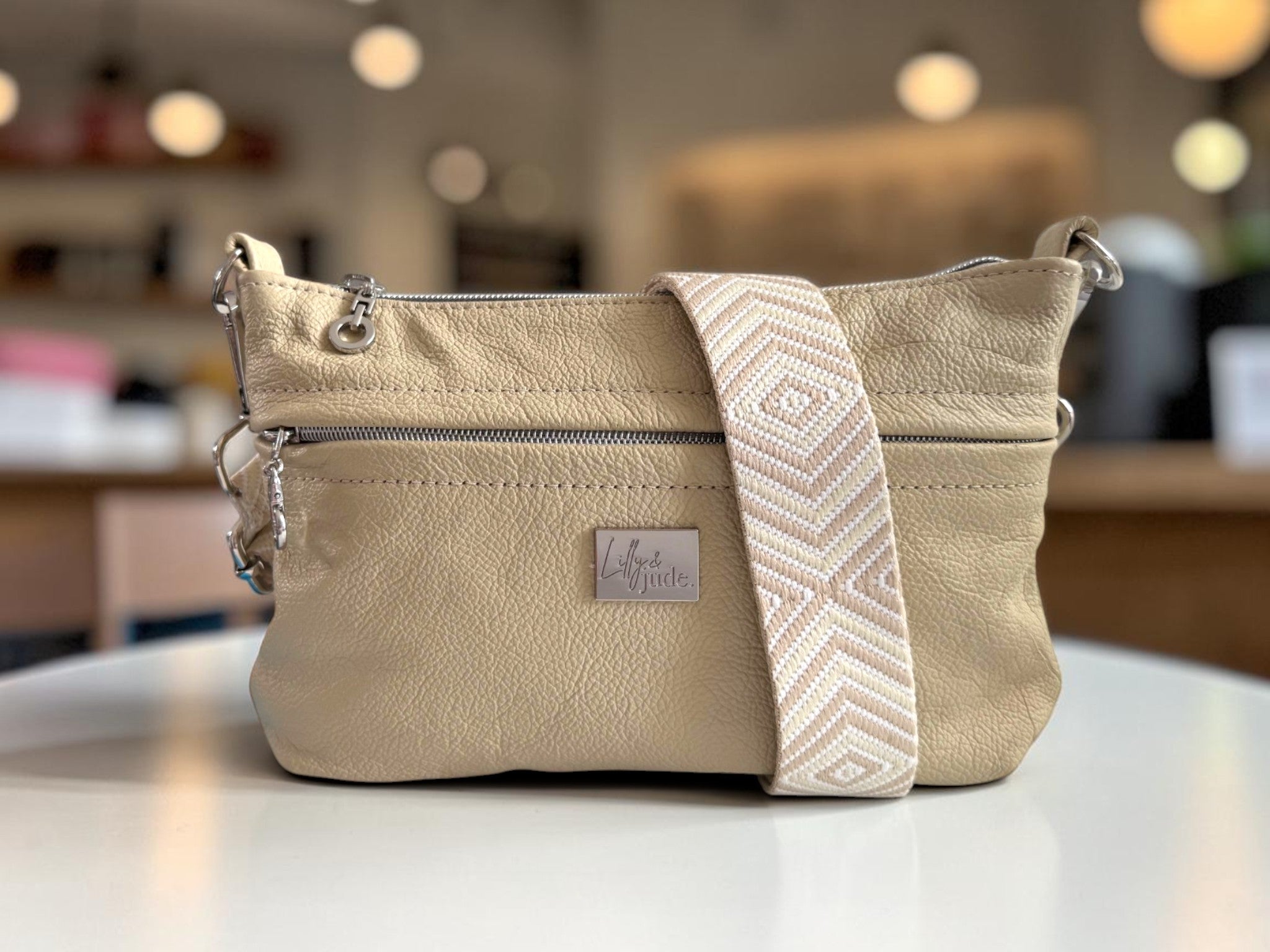 Beige handbag with a patterned strap on a blurred indoor background