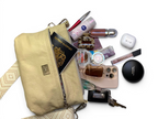 Butter yellow crossbody bag with travel essentials including a passport, phone, and cosmetics on a white background