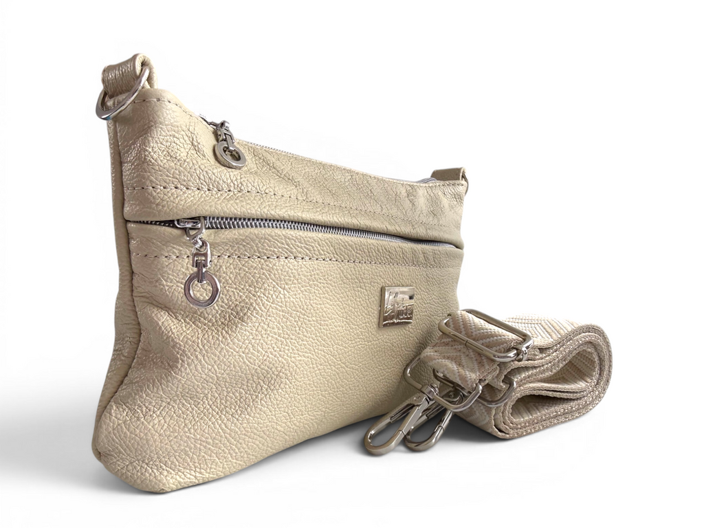 Side quarter view of the Starburn crossbody bag, made from cream full grain leather, highlighting the silver zipper pulls,  with a strap on a white background 
