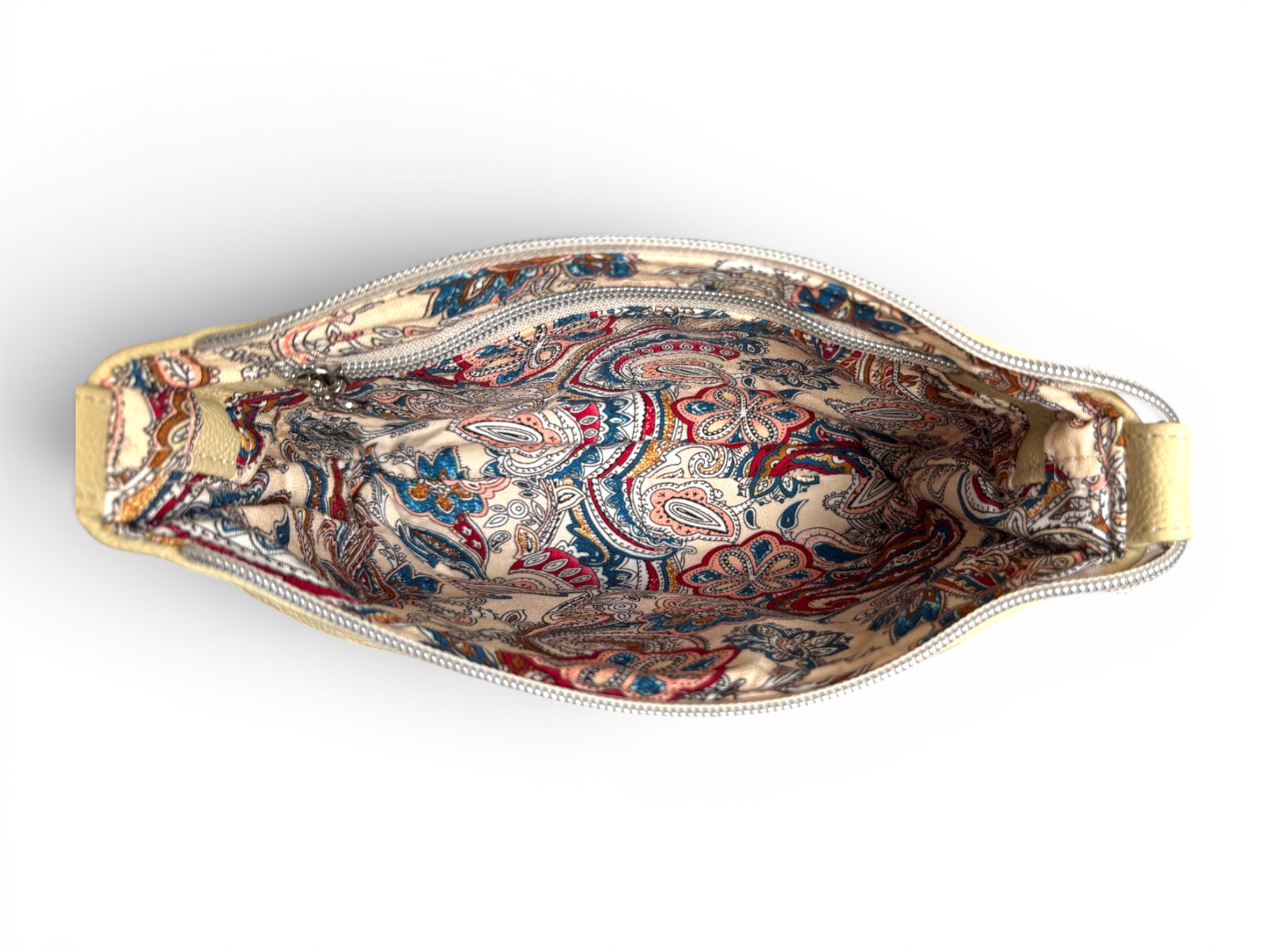 Birds eye view of the top of a butter yellow, full grain leather bag, showing the cream, blue and burgundy paisley patterned lining inside