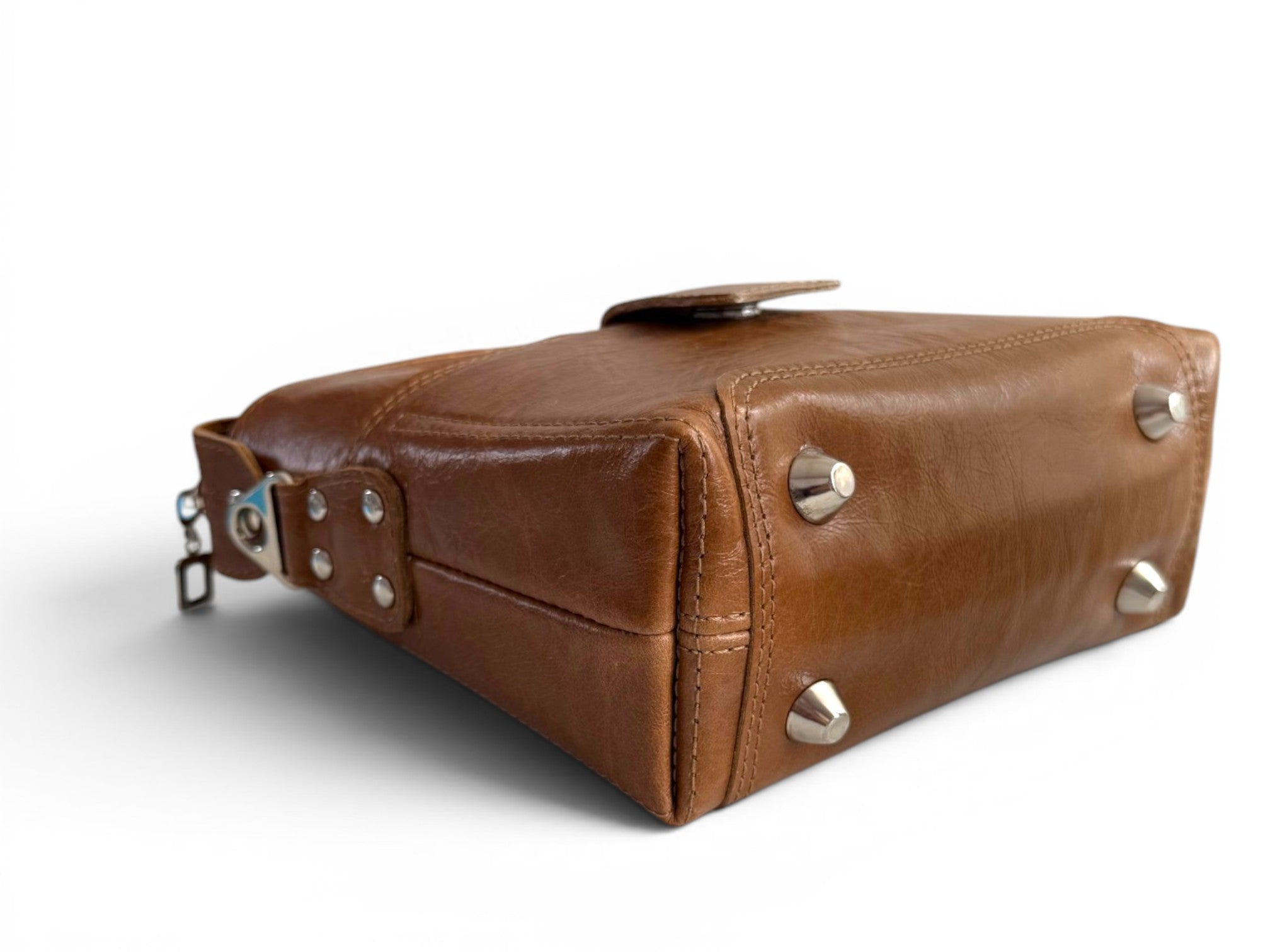 View of the bottom of a tan brown leather bag with silver stud bag feet on a white background