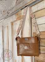 Tan brown leather handbag with a patterned strap hanging on a wooden door.