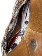 Close-up of the inside of a front pocket of a tan  brown leather bag with floral interior lining and visible brand name.