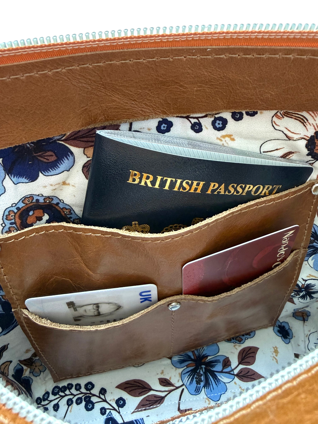View of the integrated slip pocket inside a tan brown leather bag, showing a British passport and cards against a floral patterned lining
