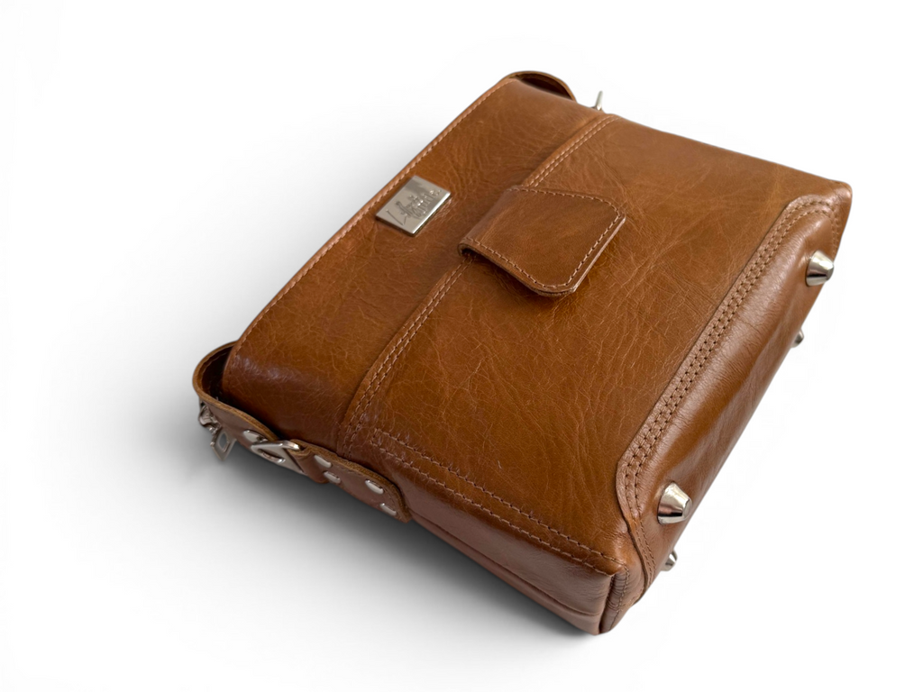 Brown leather crossbody bag with silver hardware accents lying down on a white background