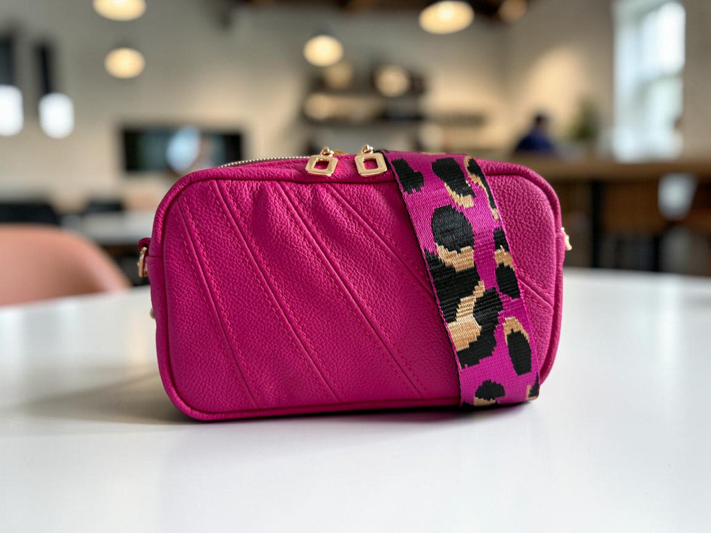 Hot pink handbag with a leopard print strap on a table in a blurred coffee shop setting