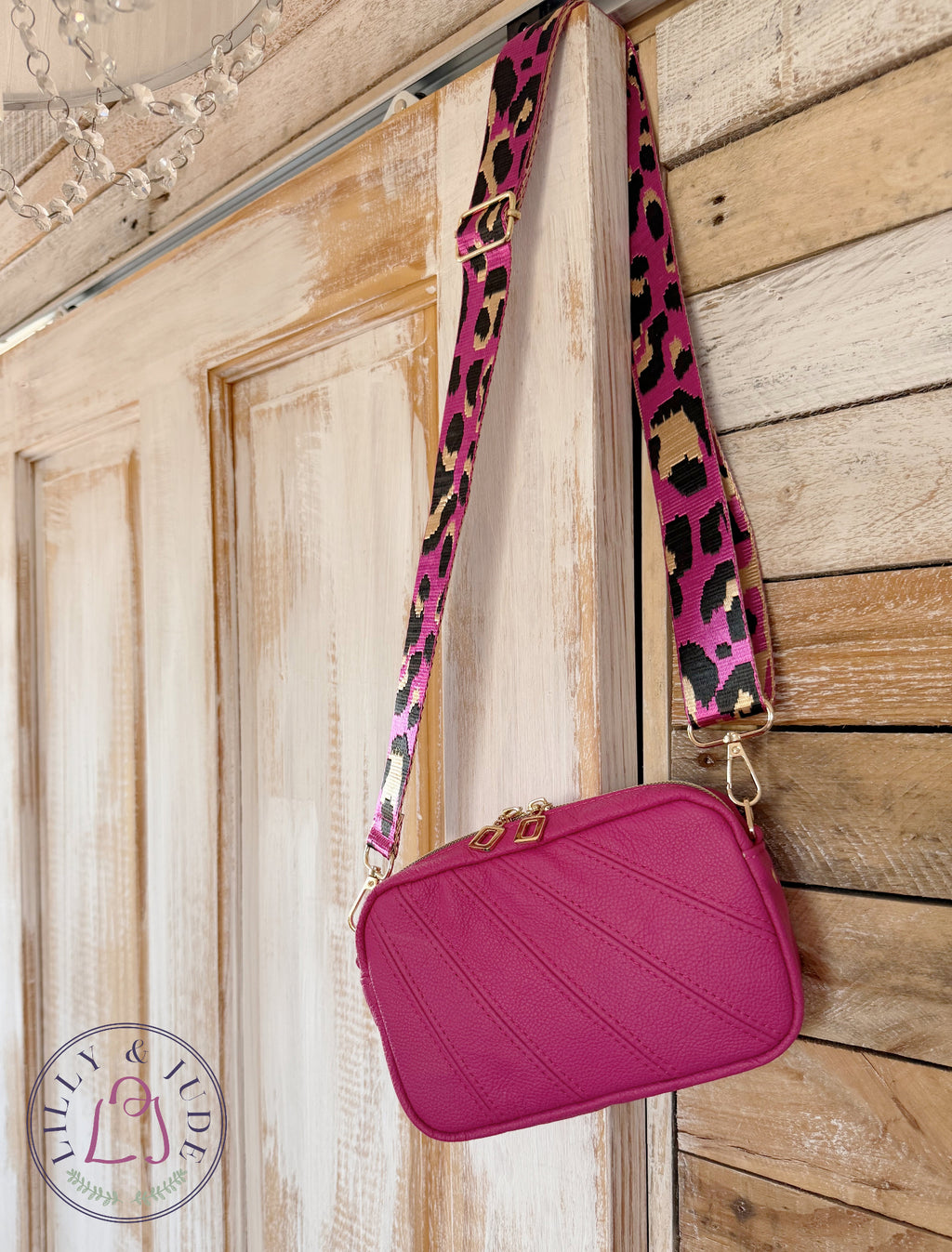 Fuschia pink compact crossbody bag with a leopard print strap hanging on a wooden door