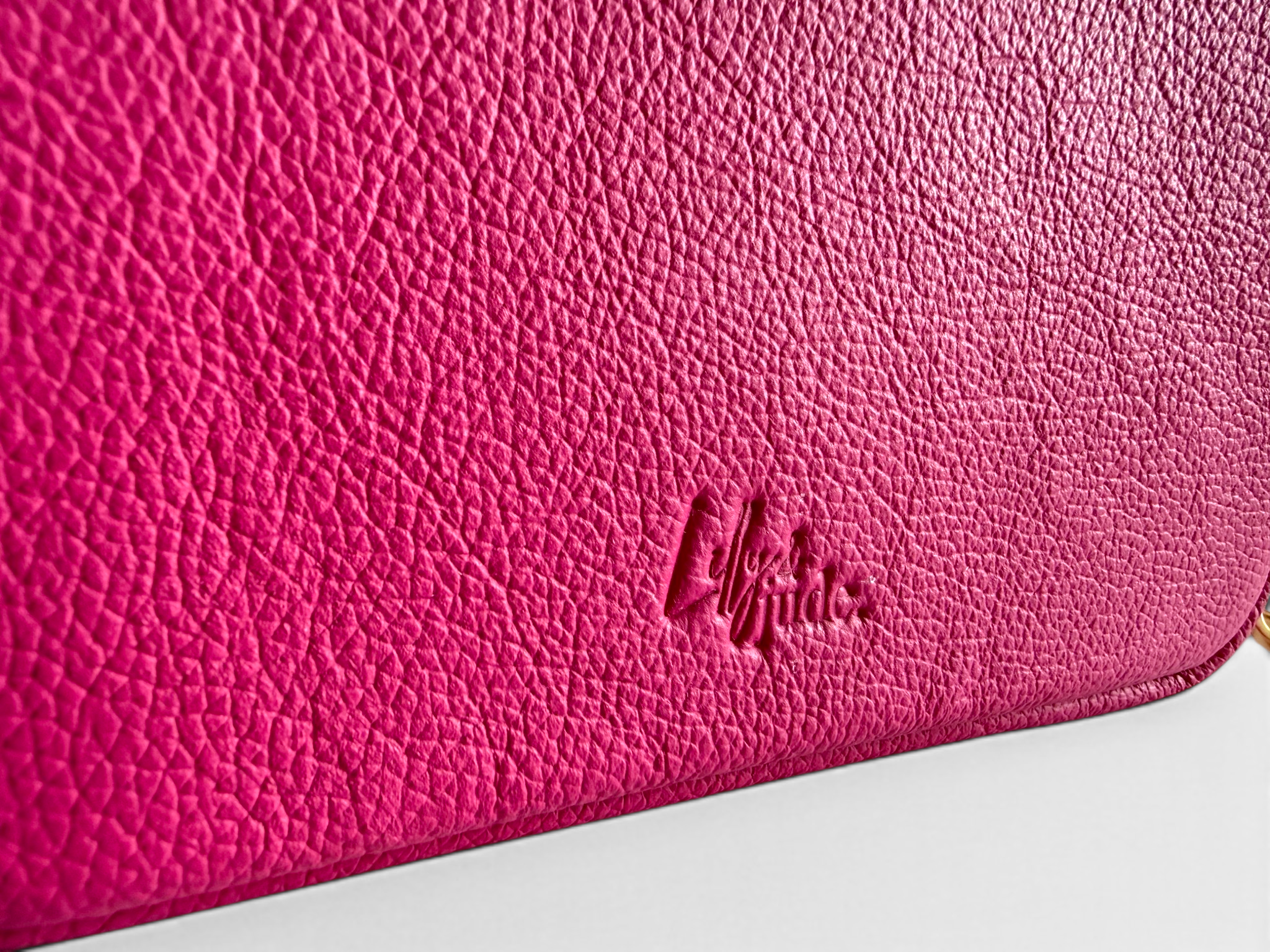 Close-up of a pink leather bag with the Lilly & Jude logo embossed into the leather, on a white background