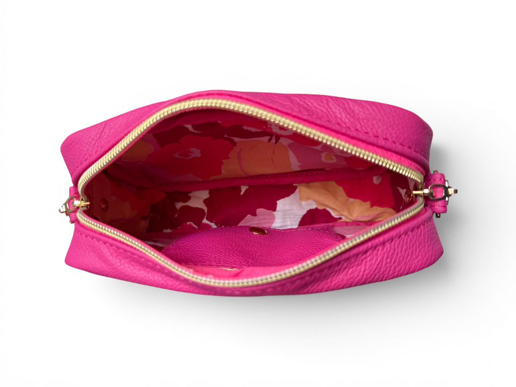 View of the top of a hot pink leather, small crossbody bag with floral interior on a white background