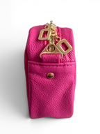 Side view of a bright pink pouch with gold zipper pull and button on a white background