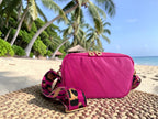 Hot pink leather, small crossbody bag with matching leopard print strap, sitting on a mat on a tropical beach