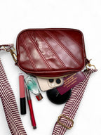 Red leather bag with makeup and travel items spilling out on a white background