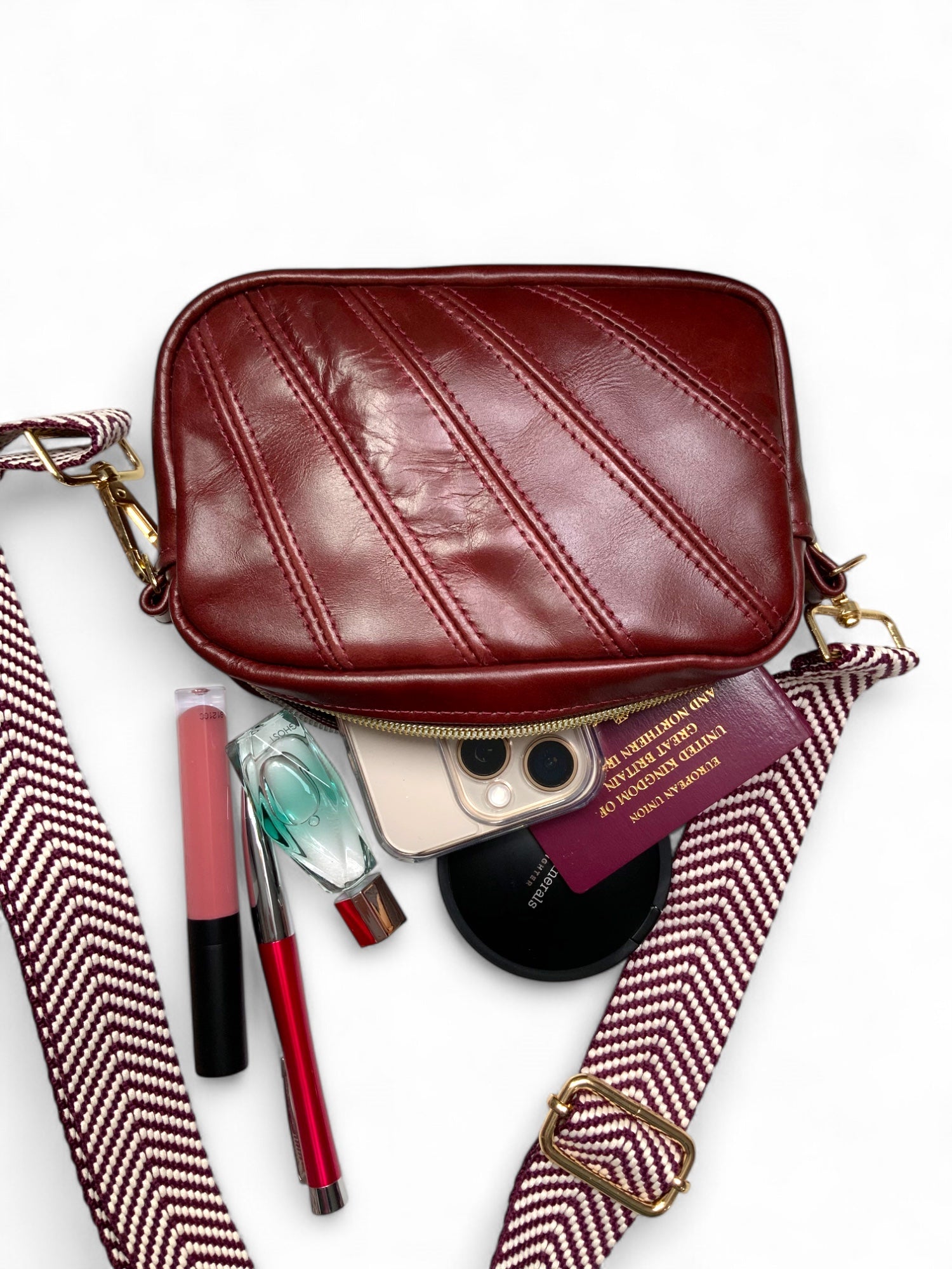Red leather bag with makeup and travel items spilling out on a white background