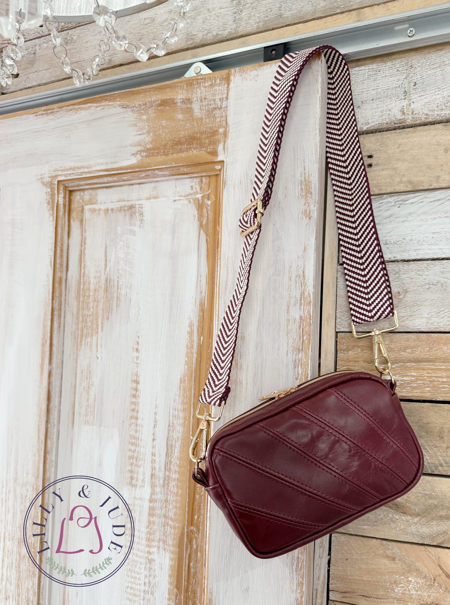 Maroon leather bag with striped strap against a distressed wooden background and Lilly & Jude logo