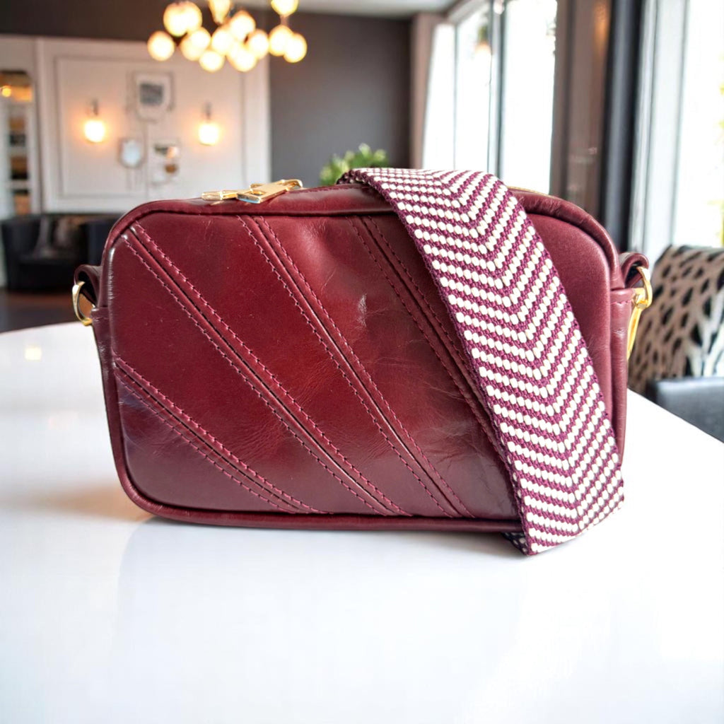 Red leather compact crossbody bag with a patterned strap on a white table.