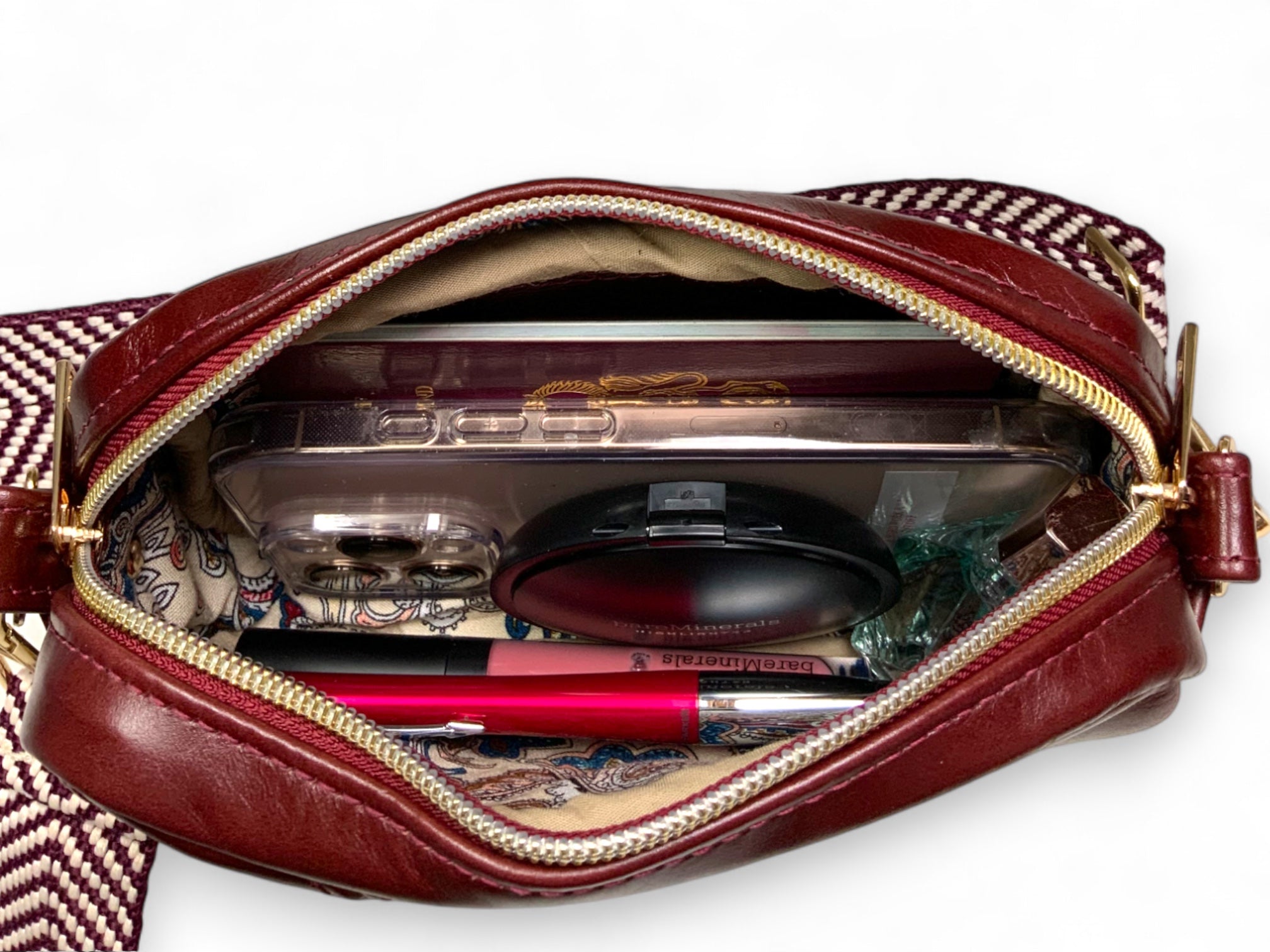 Open maroon leather handbag with contents on a white background