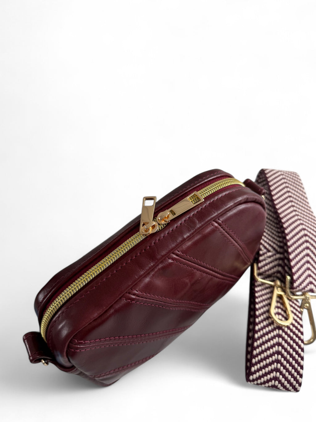 Burgundy leather bag with gold zipper and matching fabric pouch on white background