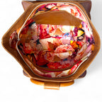 Interior view of the floral-patterned lining fabric inside a tan coloured leather bag on a white background.