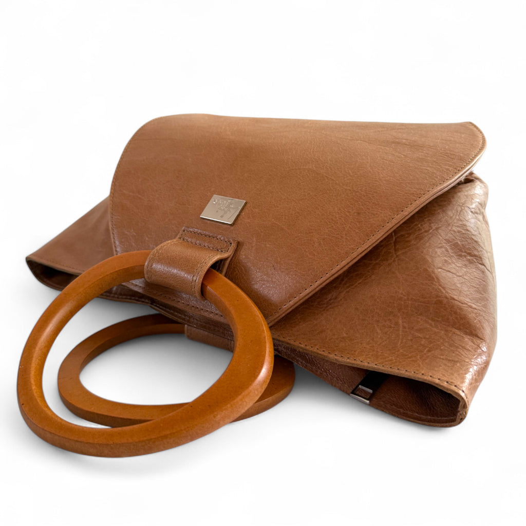 Tan brown leather handbag by Lilly & Jude, with wooden handles, lying on a white background. 