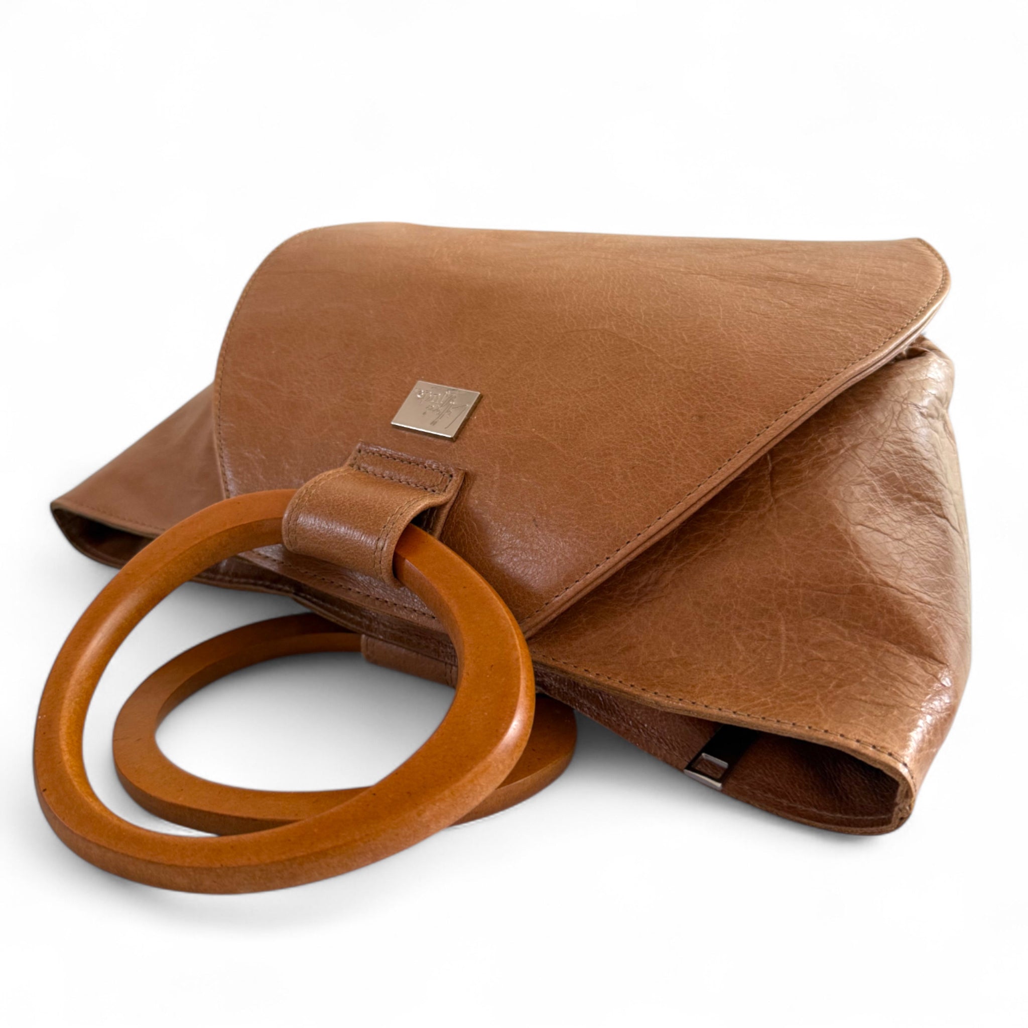 Tan brown leather handbag by Lilly & Jude, with wooden handles, lying on a white background. 