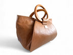The front quarter view of a tan brown leather handbag with wooden handles and emphasises the unique design. 