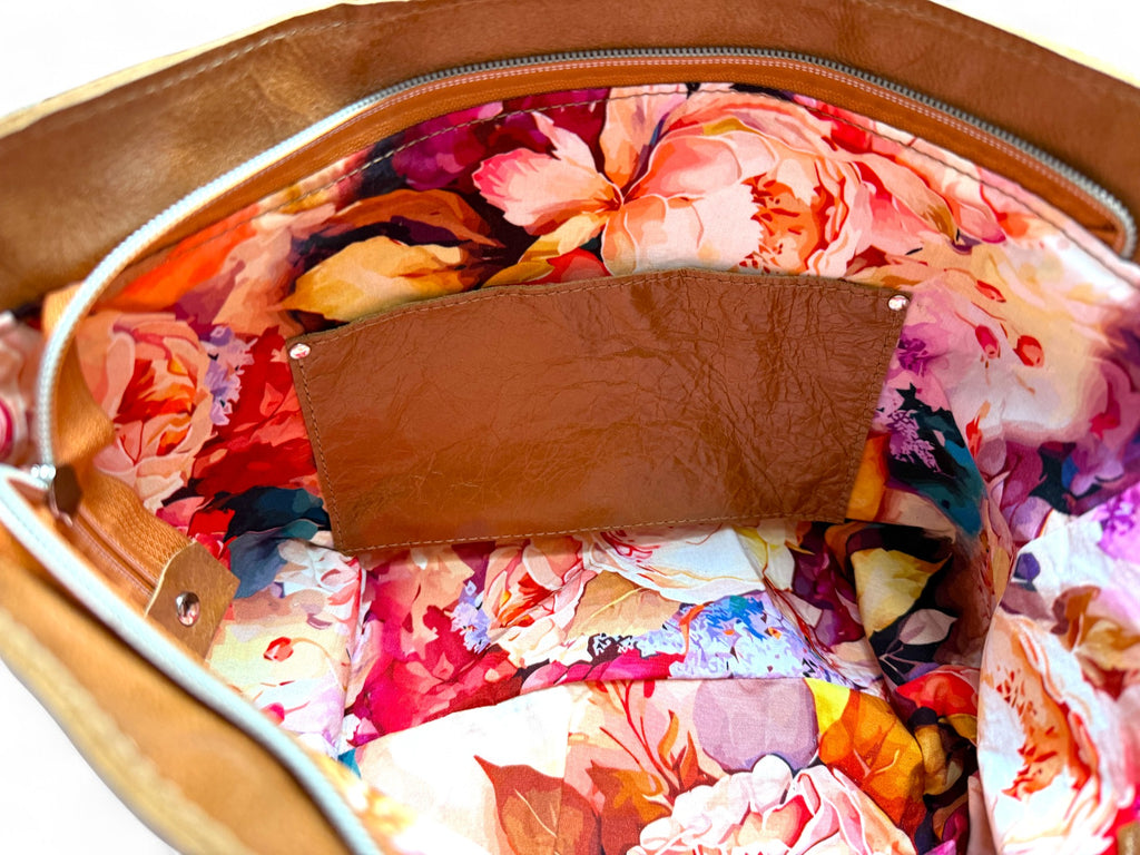 Interior view of the inside of the bag showing the colourful, floral lining and the matching tan leather slip pocket. 