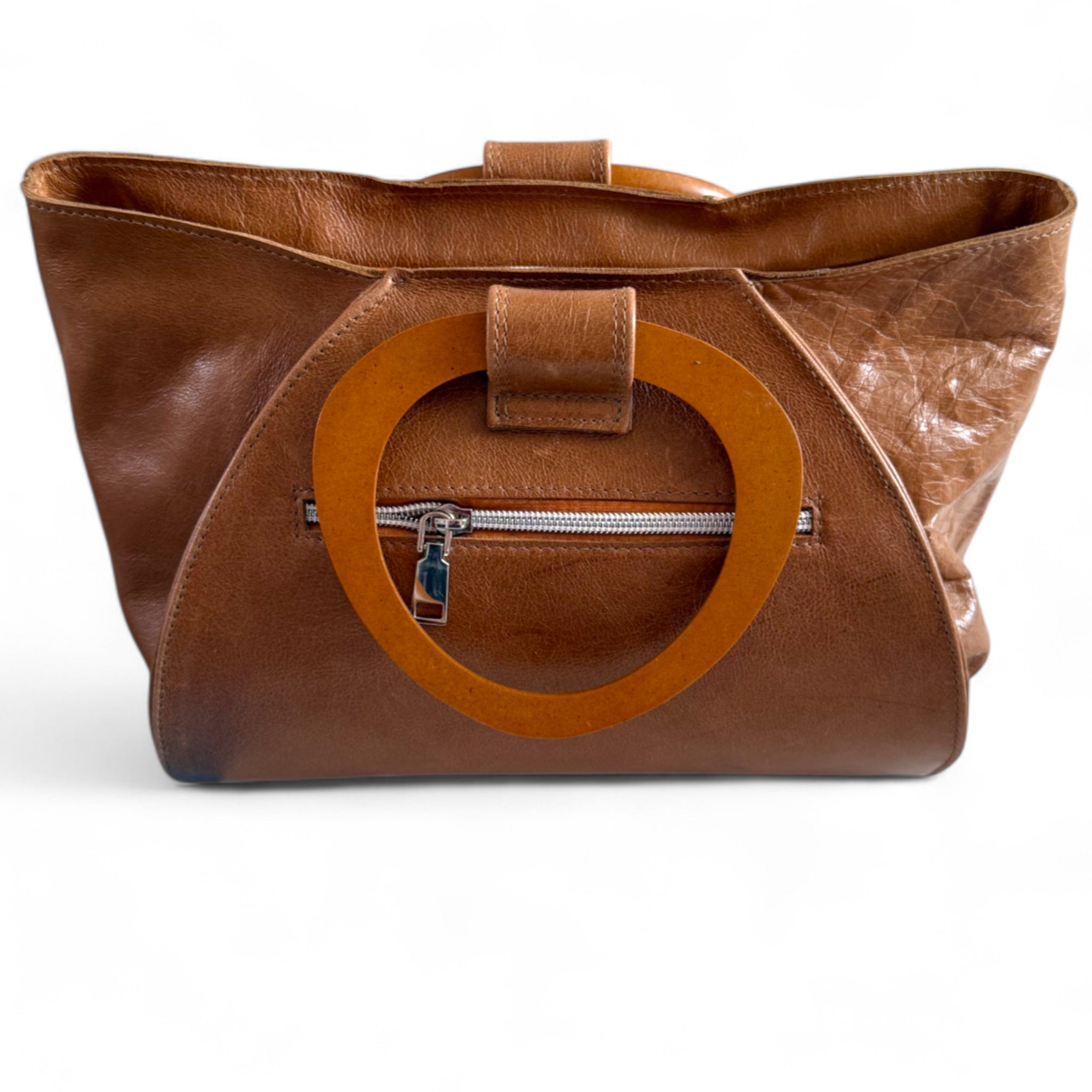 View of the back of a tan leather handbag with wooden handles, and zipper pocket, sitting on a white background.