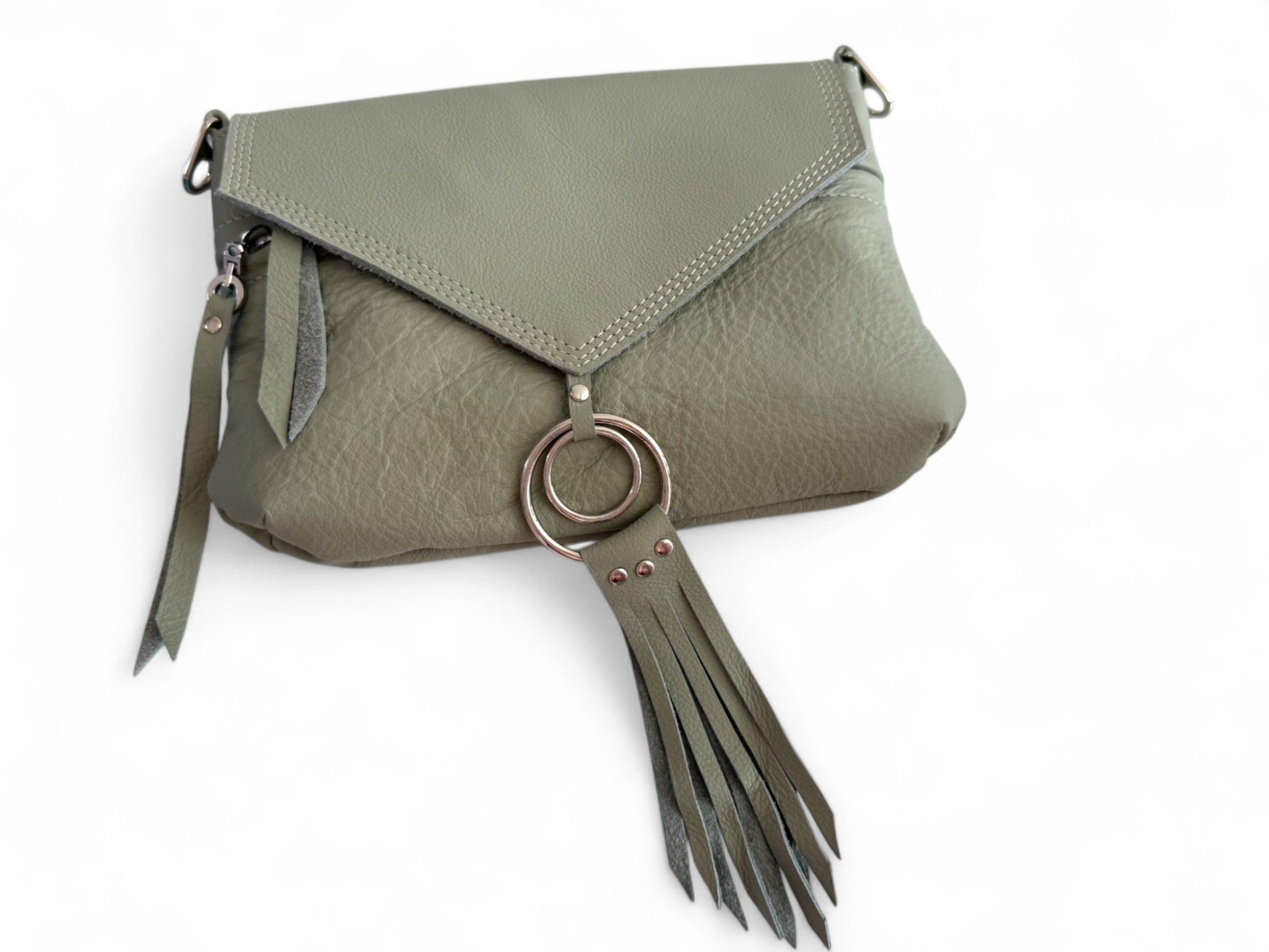 Pale olive green bag lying on a white background. The image shows the triangular shape of the flap and the detail of the silver rings and tassel that are attached to the flap. This bag is called Olivia and is hand made from eco-conscious materials, including genuine leather that was rescued from heading to landfill 
