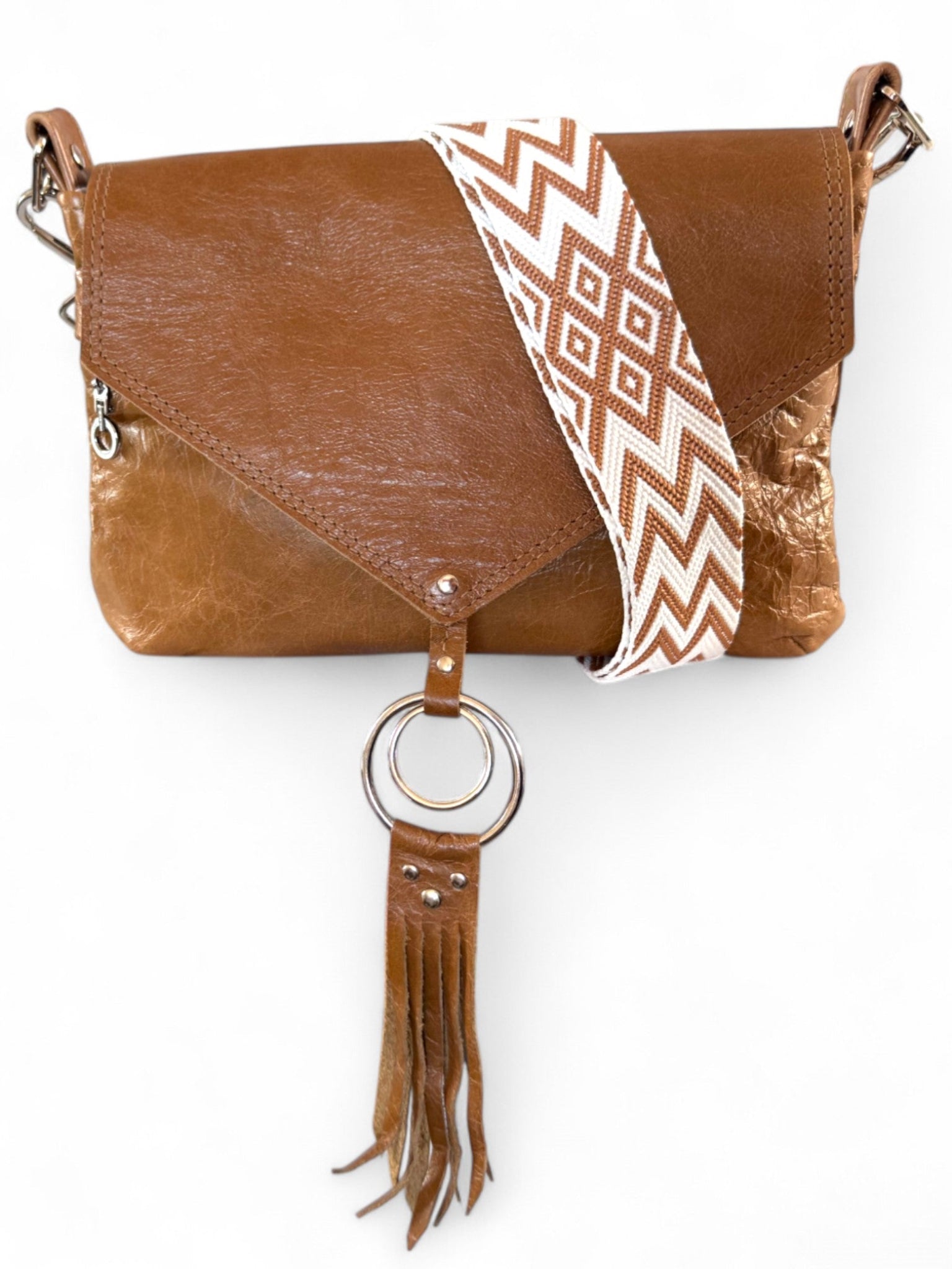 Tan brown, rescued leather crossbody bag with an envelope shaped flap. Draped over the top of the bag is a matching woven, chevron patterned, crossbody strap. The image also shows the fringe detail and the bag is on a white background
