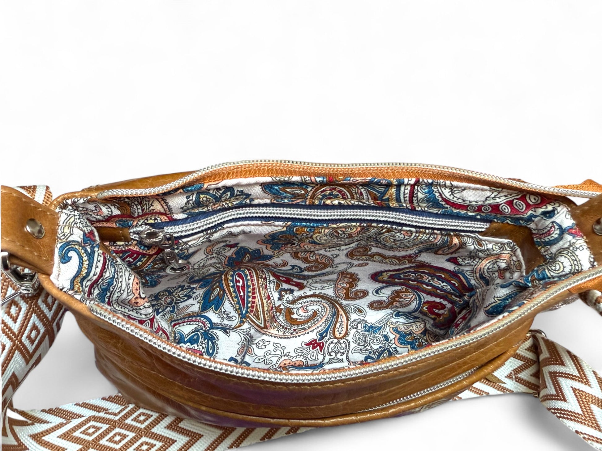 View from above of a tan coloured Olivia crossbody bag, opened and showing the beautiful paisley patterned lining and the interior zipper. The bag is sat on a white background 