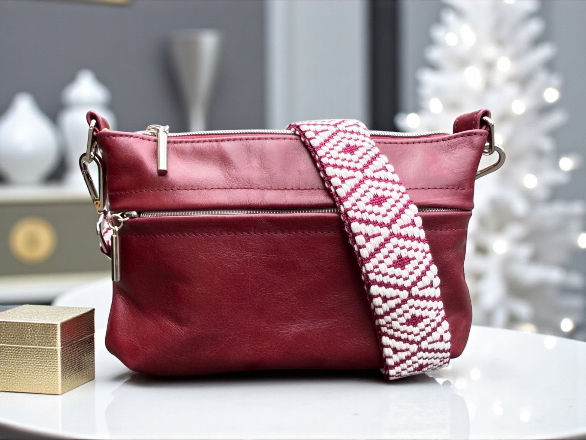 Burgundy leather bag in a boutique with a Christmas tree in the background and a small gold gift box. 