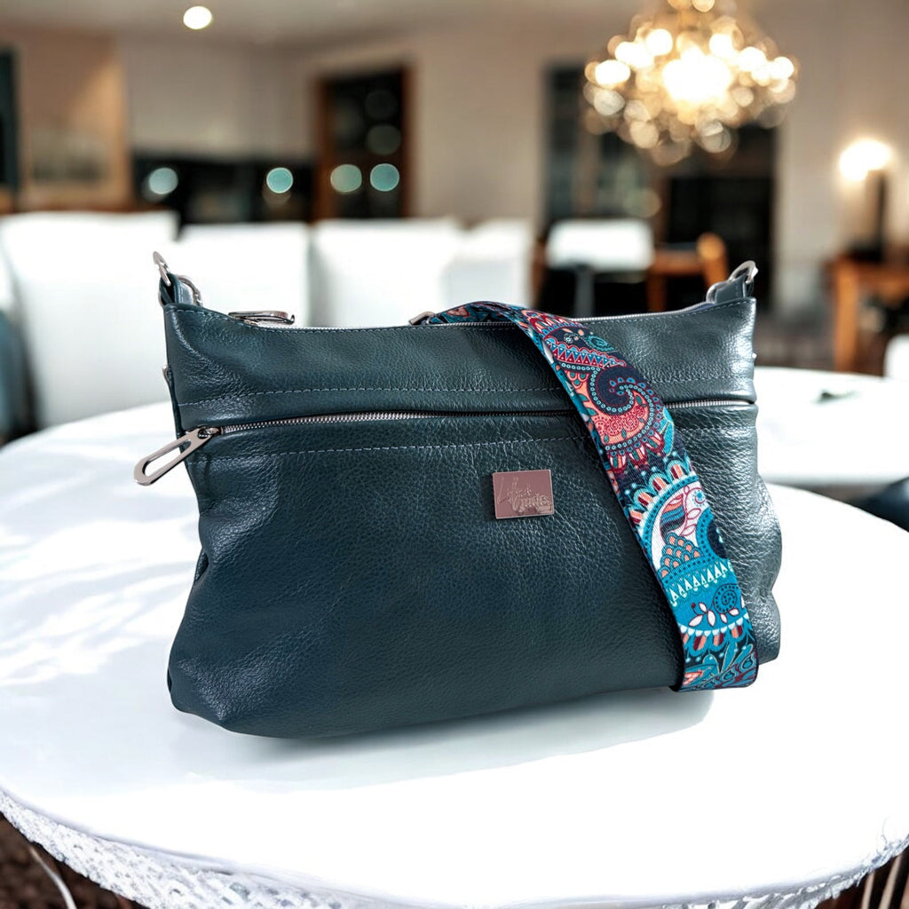 Dark green leather bag with a colorful strap on a white table in a blurred indoor background.