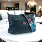 Dark green leather bag with a colorful strap on a white table in a blurred indoor background.