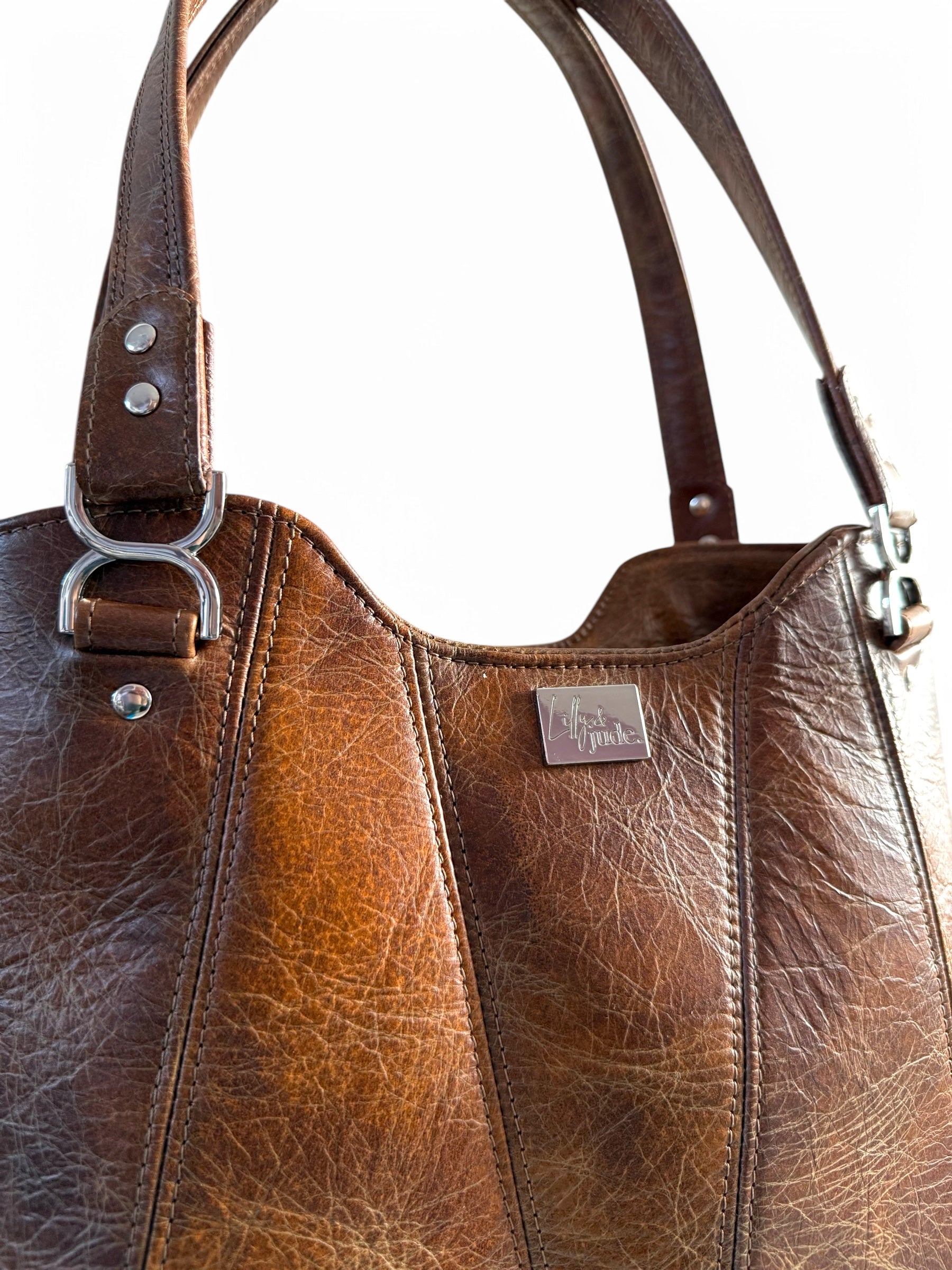 Close-up of brown Alaula leather bag showing detailed stitching, silver hardware, and metal Lilly & Jude logo tag